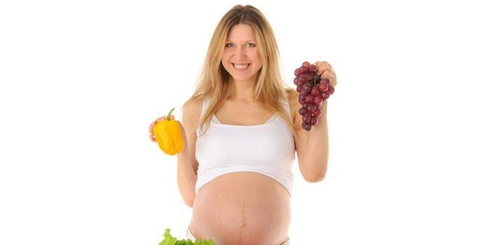 Беременная женщина держит перец и гроздь винограда в руках